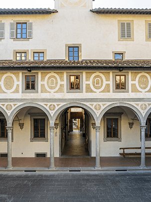 Il loggiato del Cortile degli Uomini dell'Istituto degli Innocenti scandito da colonne e arcate. Al primo piano lungo le pareti si alternano finestre e decorazioni a grafitto