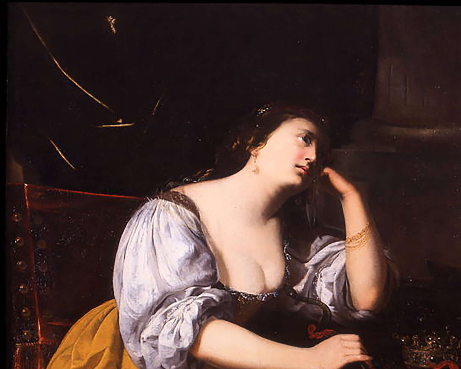 Figura seduta con abito azzurro e giallo, appoggiata a un tavolo con un gioiello; illuminazione drammatica su sfondo scuro tipica della pittura barocca.