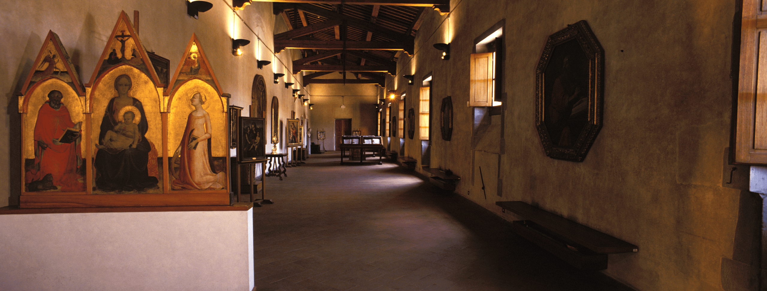 Storica Pinacoteca degli Innocenti con polittico a fondo oro, dipinti e vetrine espositive in una lunga galleria illuminata.