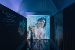 An immersive corridor bathed in blue light, featuring Artemisia Gentileschi’s *Allegory of Inclination* projected onto a curtain of threads.