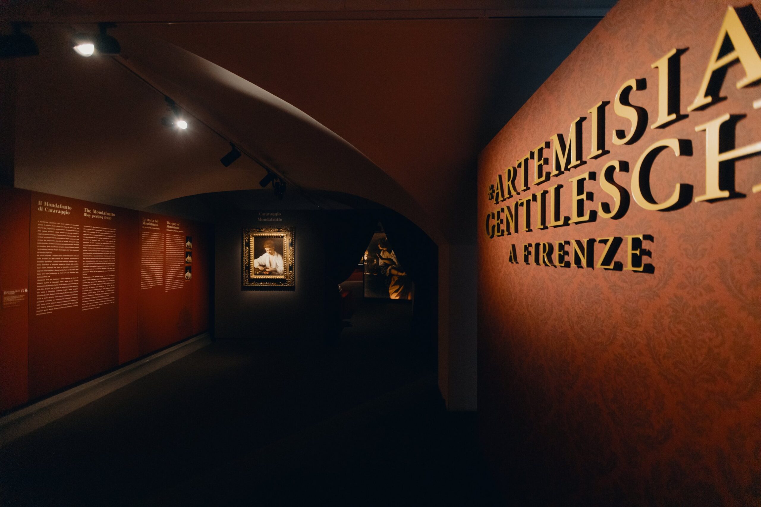 Entrance to the exhibition titled “Artemisia Gentileschi in Florence,” with the title written in gold letters on a red damask-patterned wall.