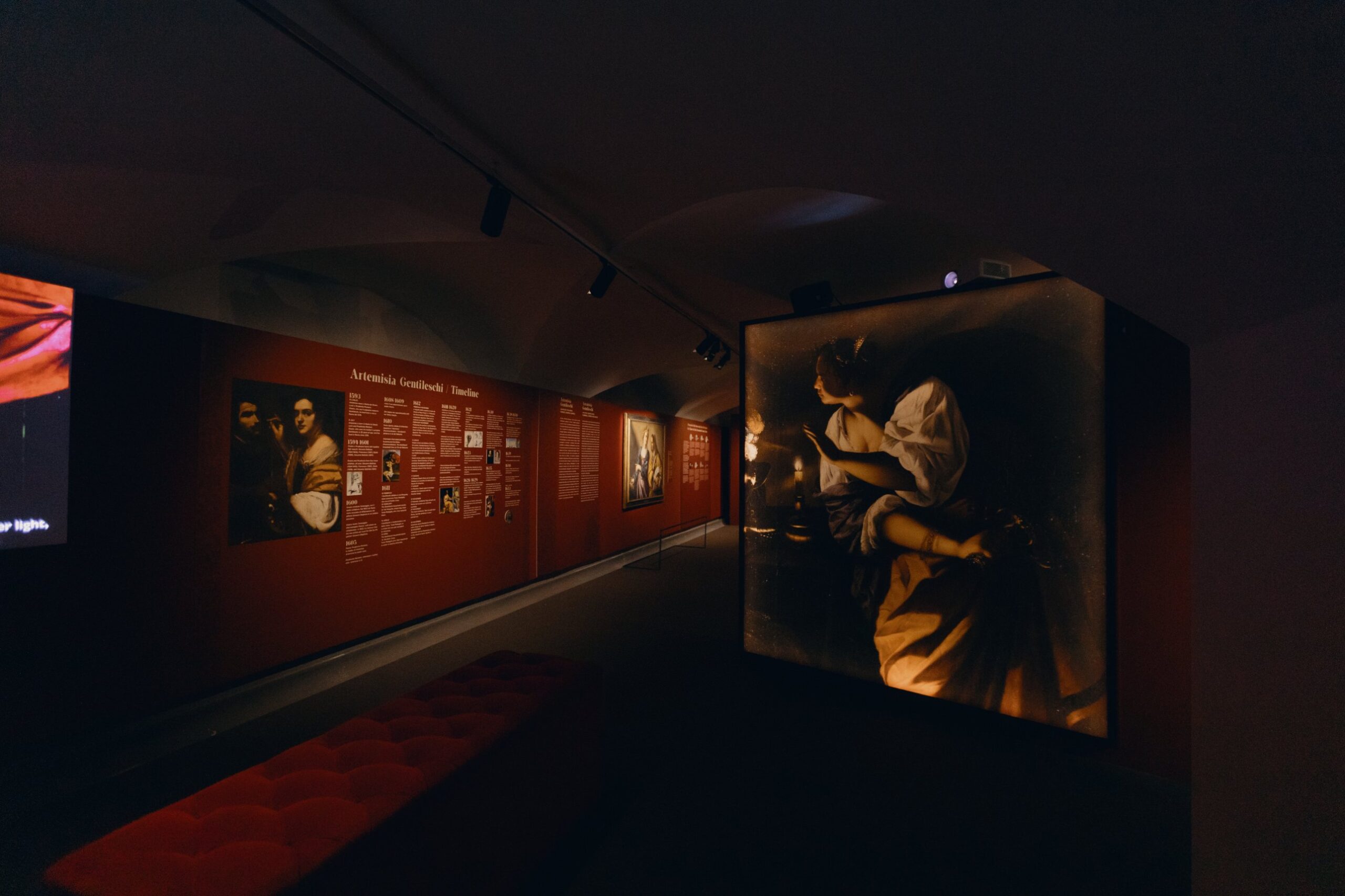 A room featuring a timeline of Artemisia's life on a red wall and a backlit panel depicting a female figure by candlelight.